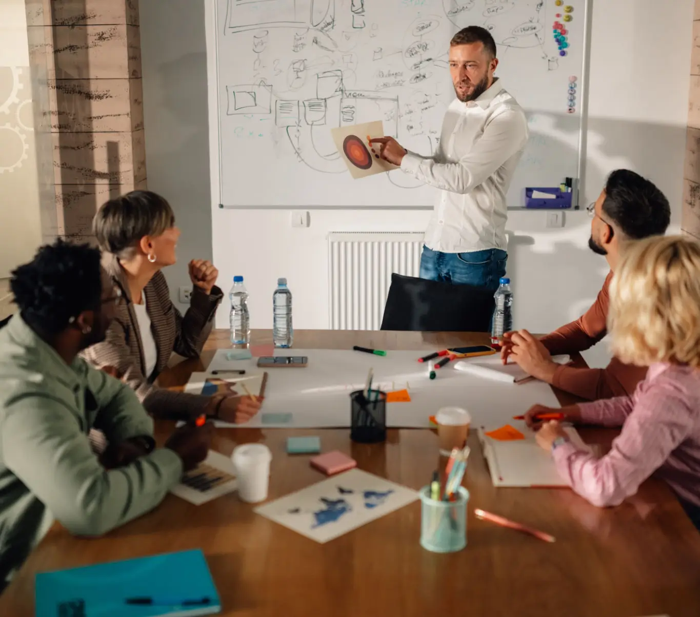 A man presents a project to colleagues in a modern office meeting.