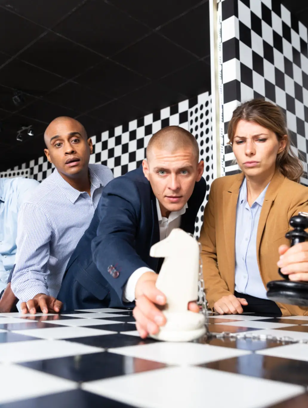 Three people intensely playing chess with a large white pawn.