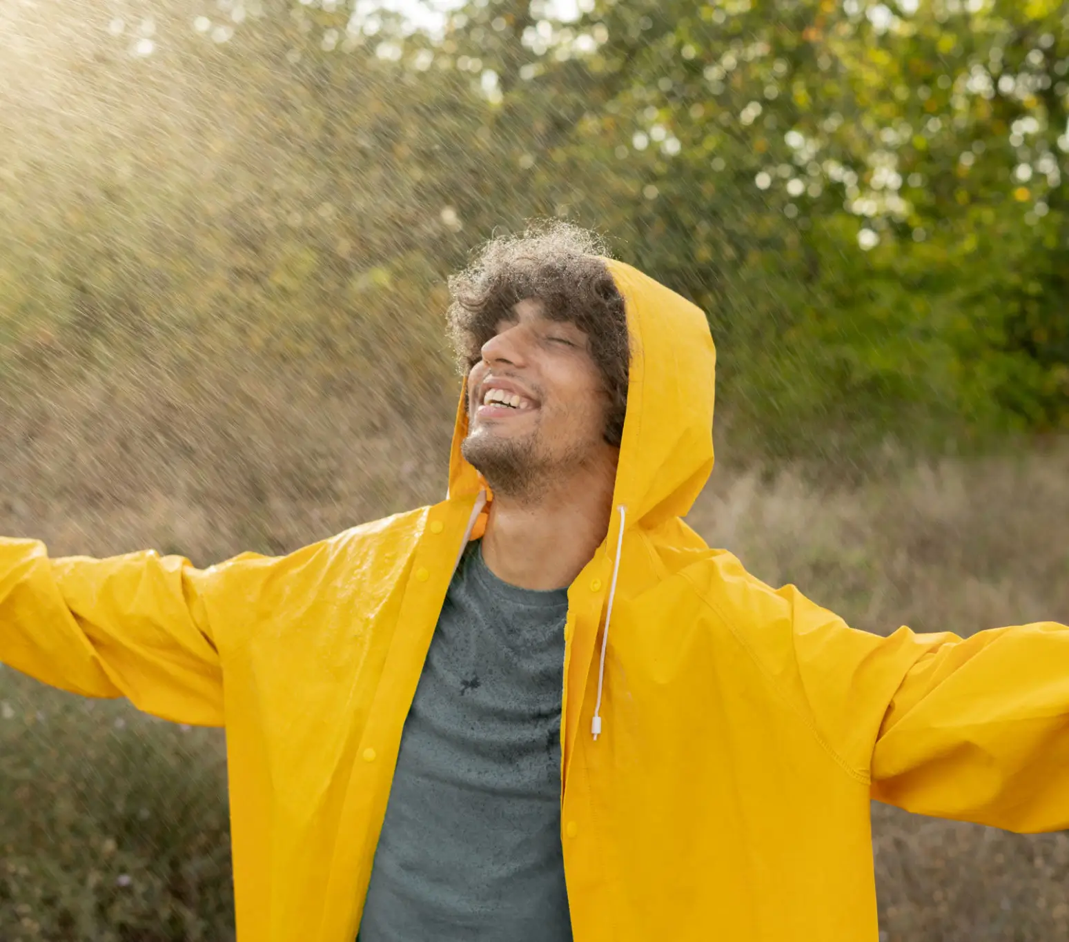 Man joyfully enjoying nature with arms outstretched in a yellow raincoat.
