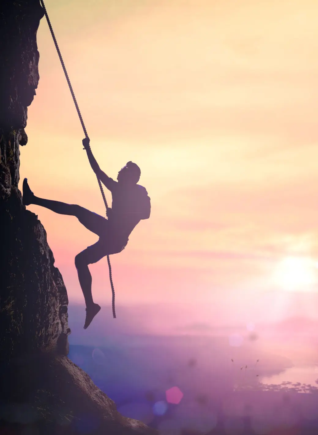 Person rock climbing during sunset with a dramatic sky.