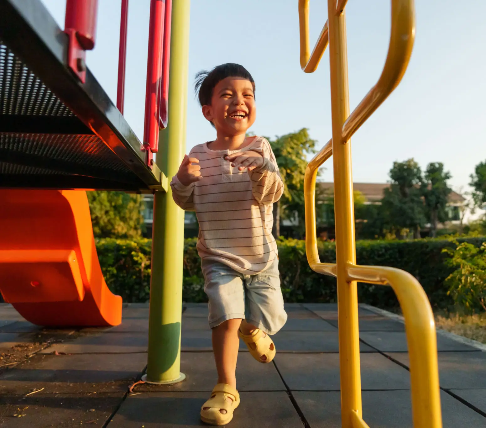 A joyful boy running on a playground structure during sunset.