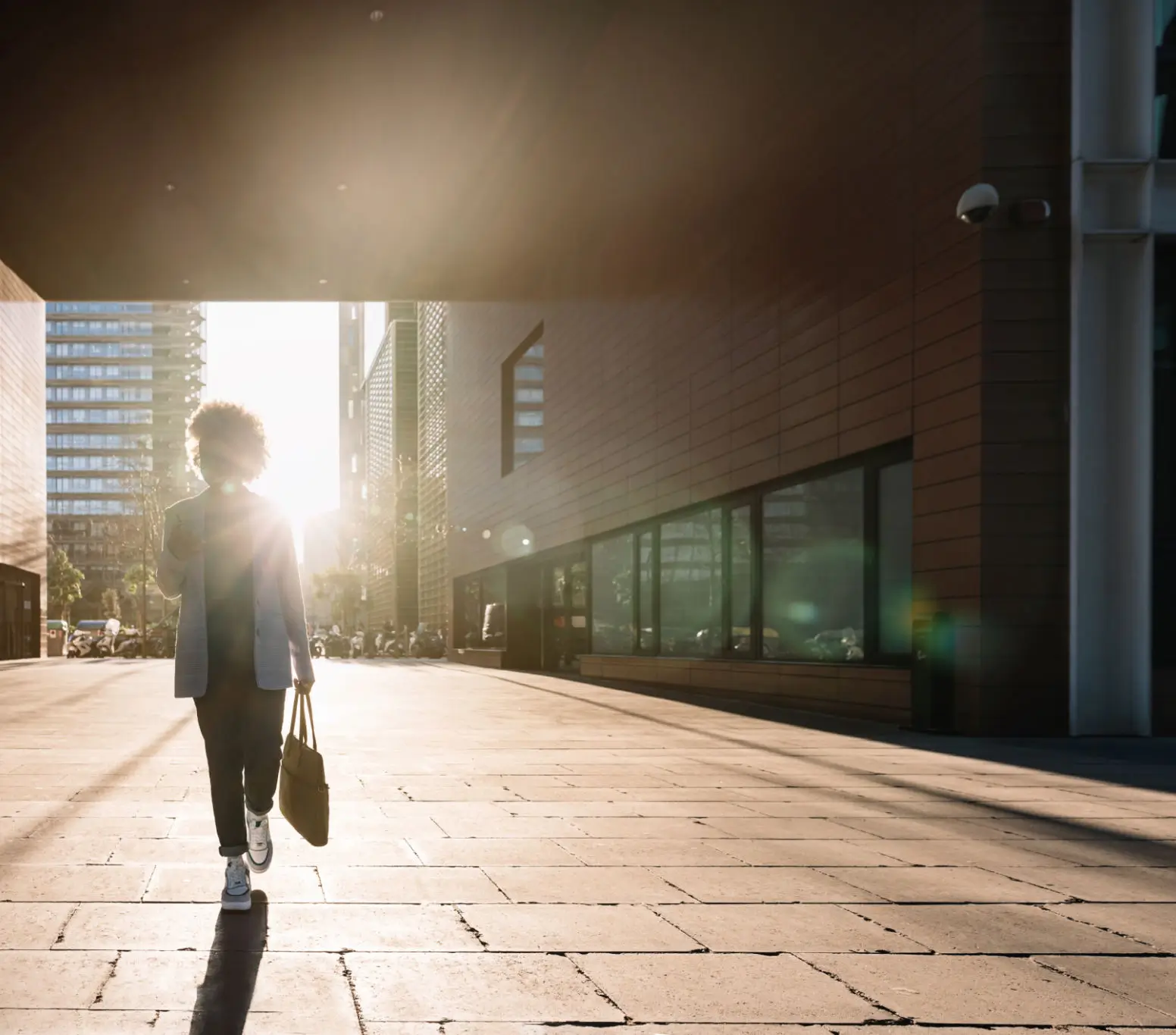 Person walking on a sunlit urban street carrying a briefcase.