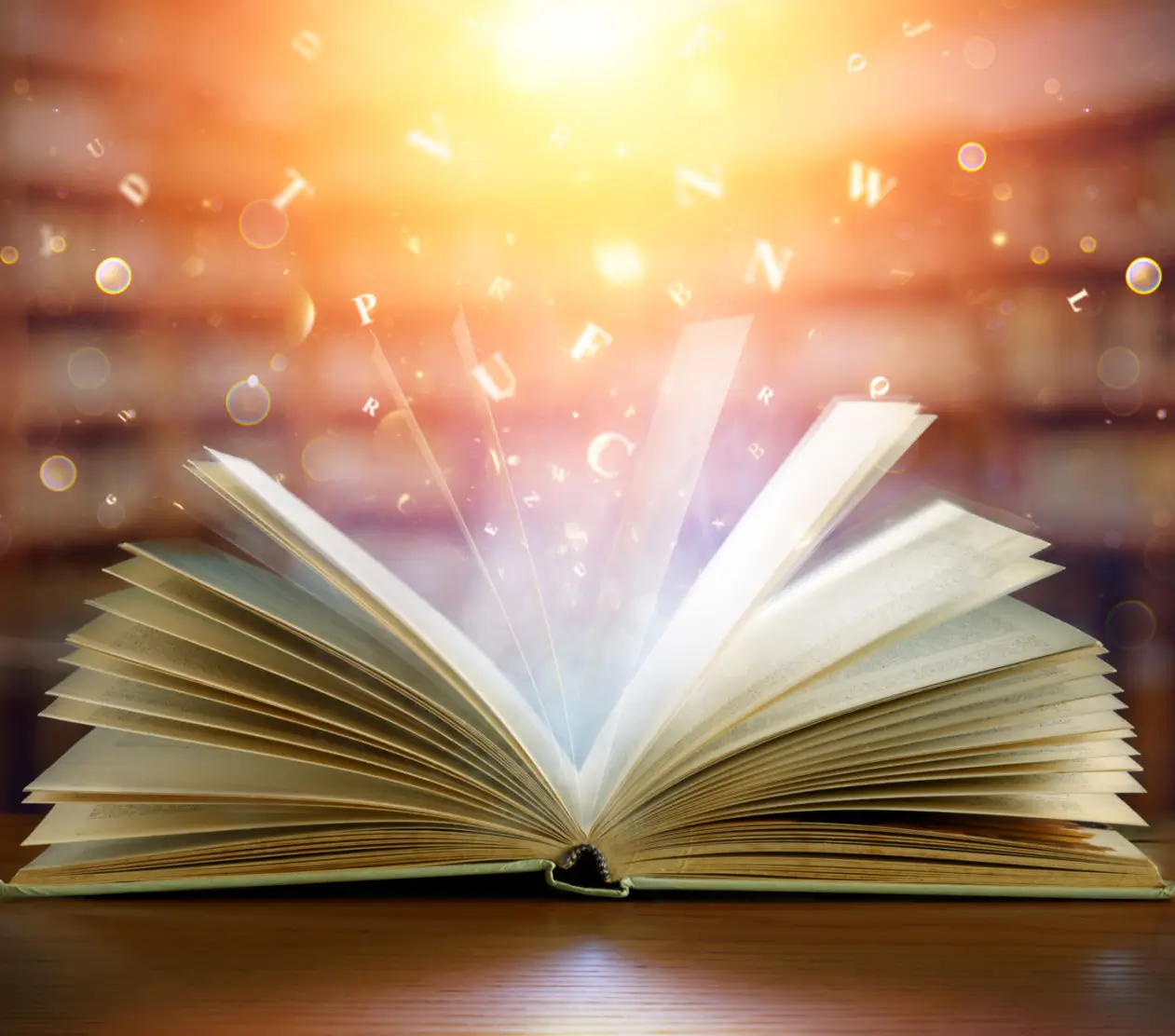 An open book glowing with magical light on a wooden surface.