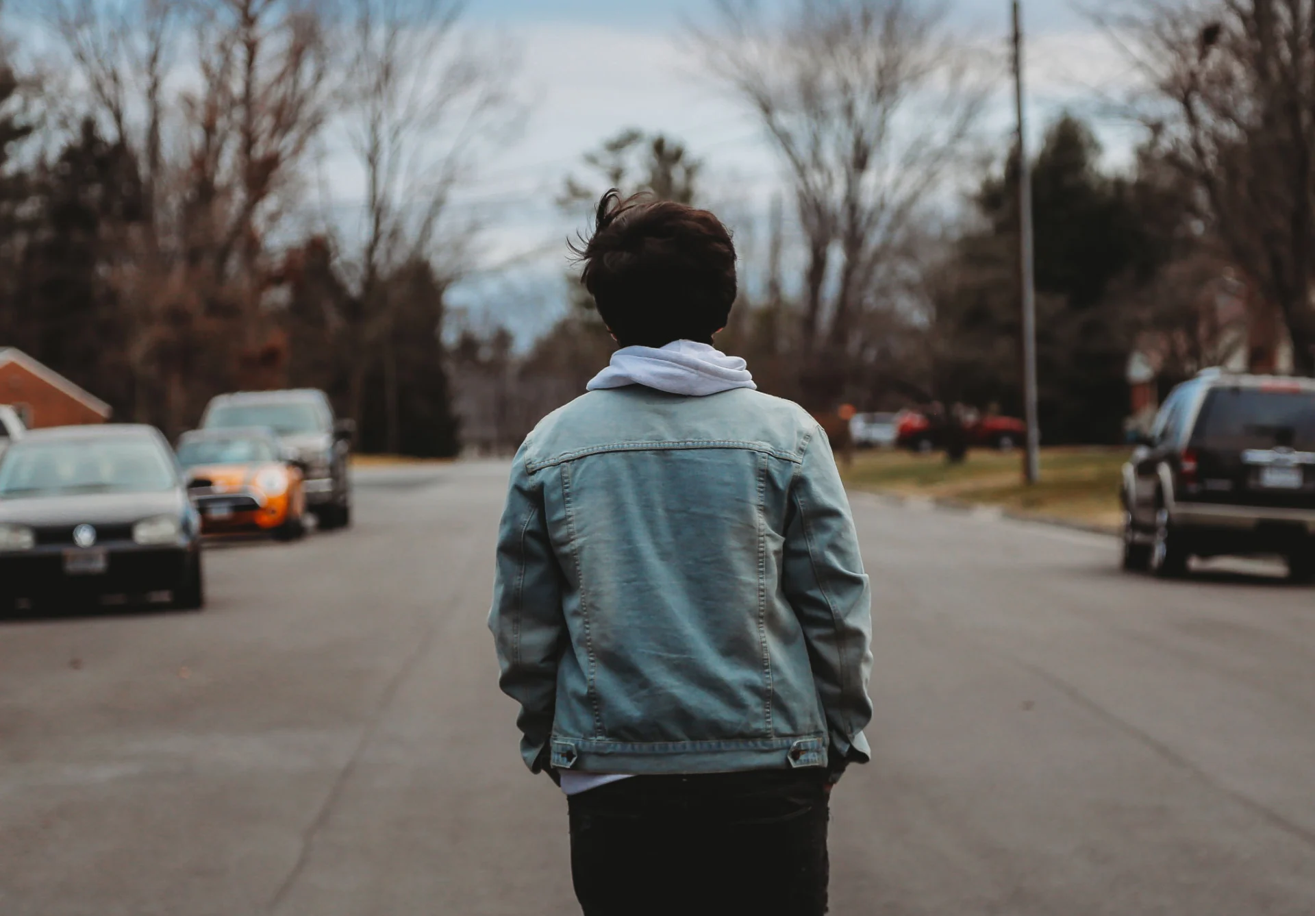 Person walking down a street wearing a denim jacket and hoodie.