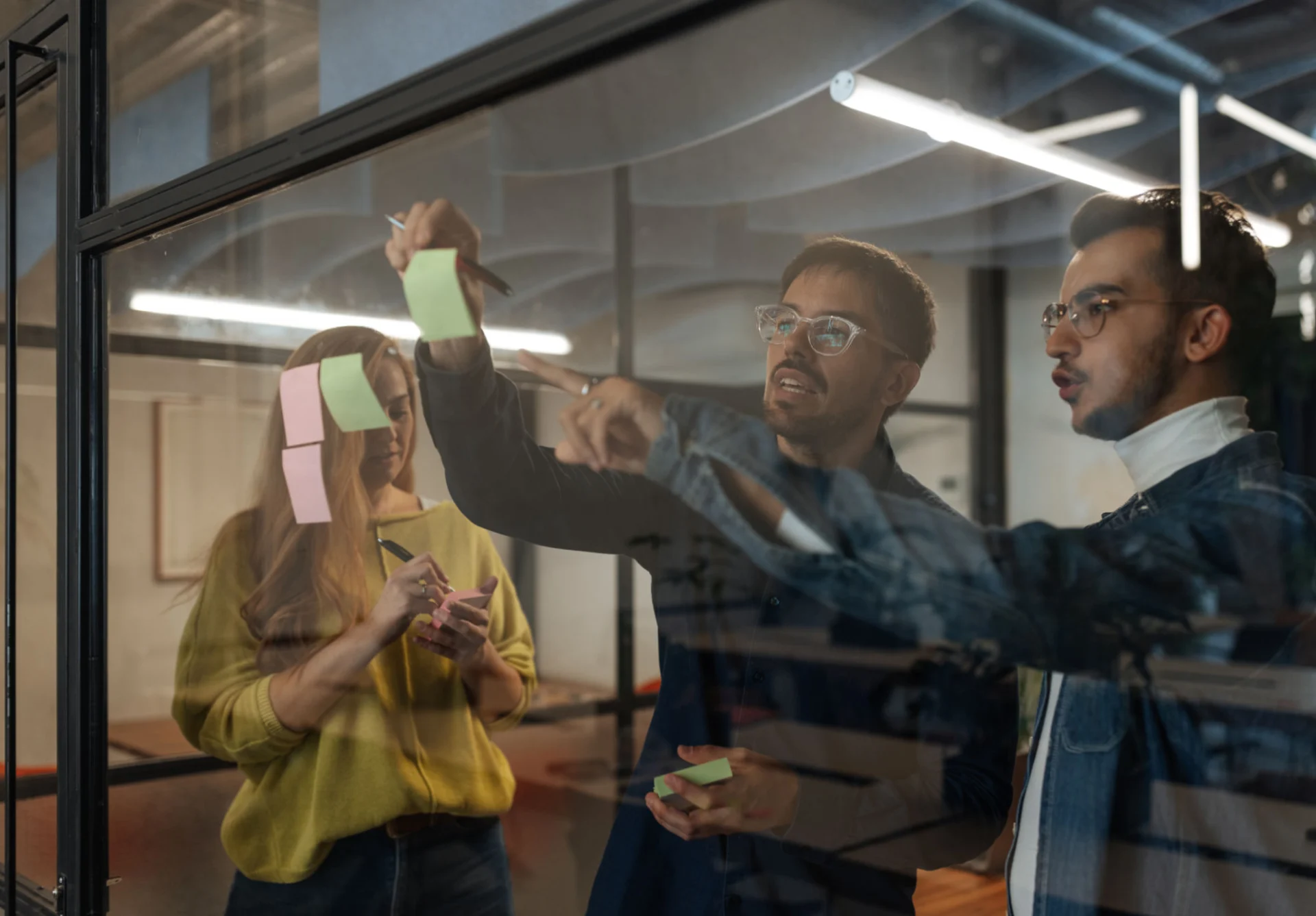 Team collaborating on ideas using sticky notes on glass.