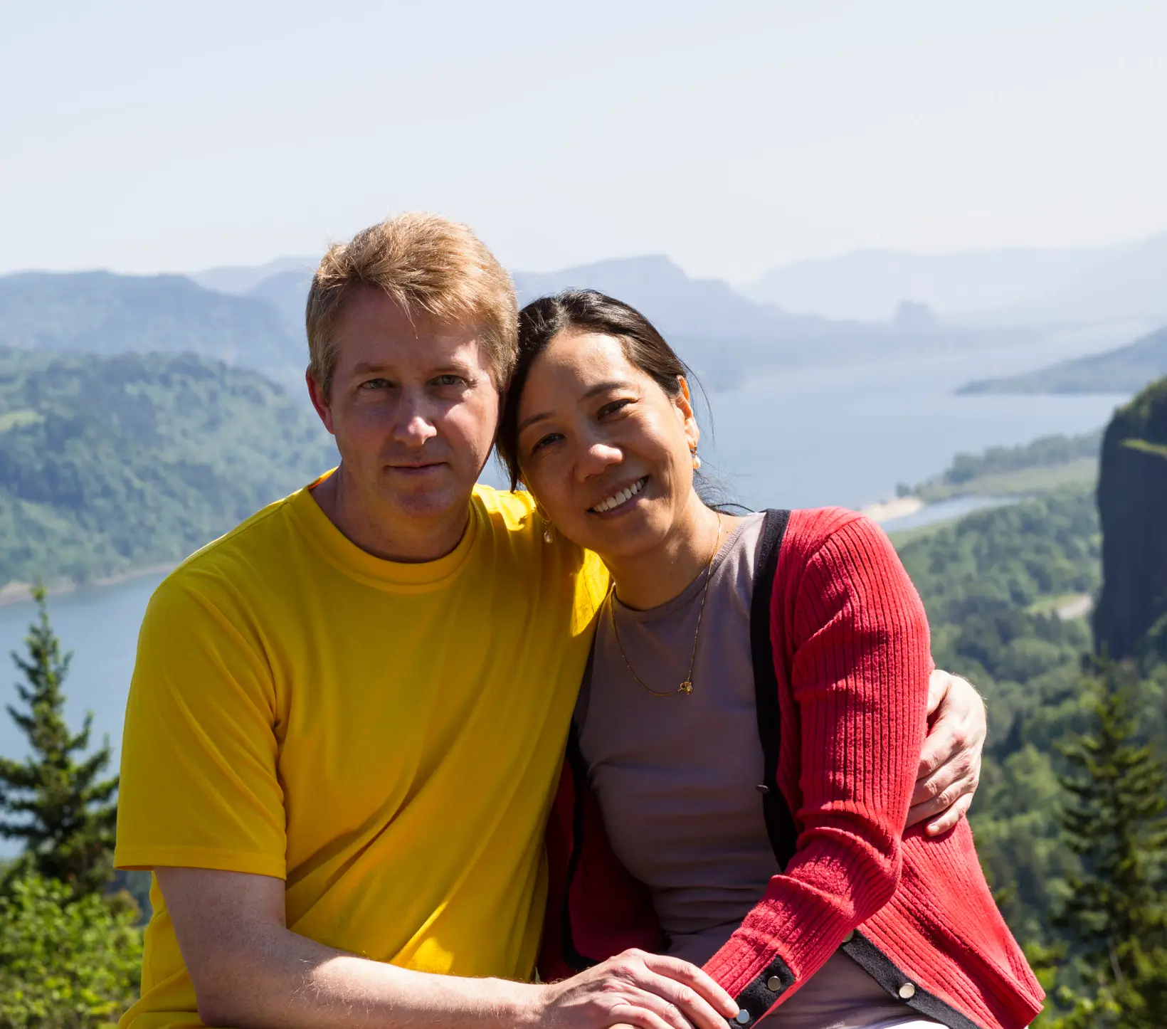 Couple posing outdoors with scenic mountain and river view.
