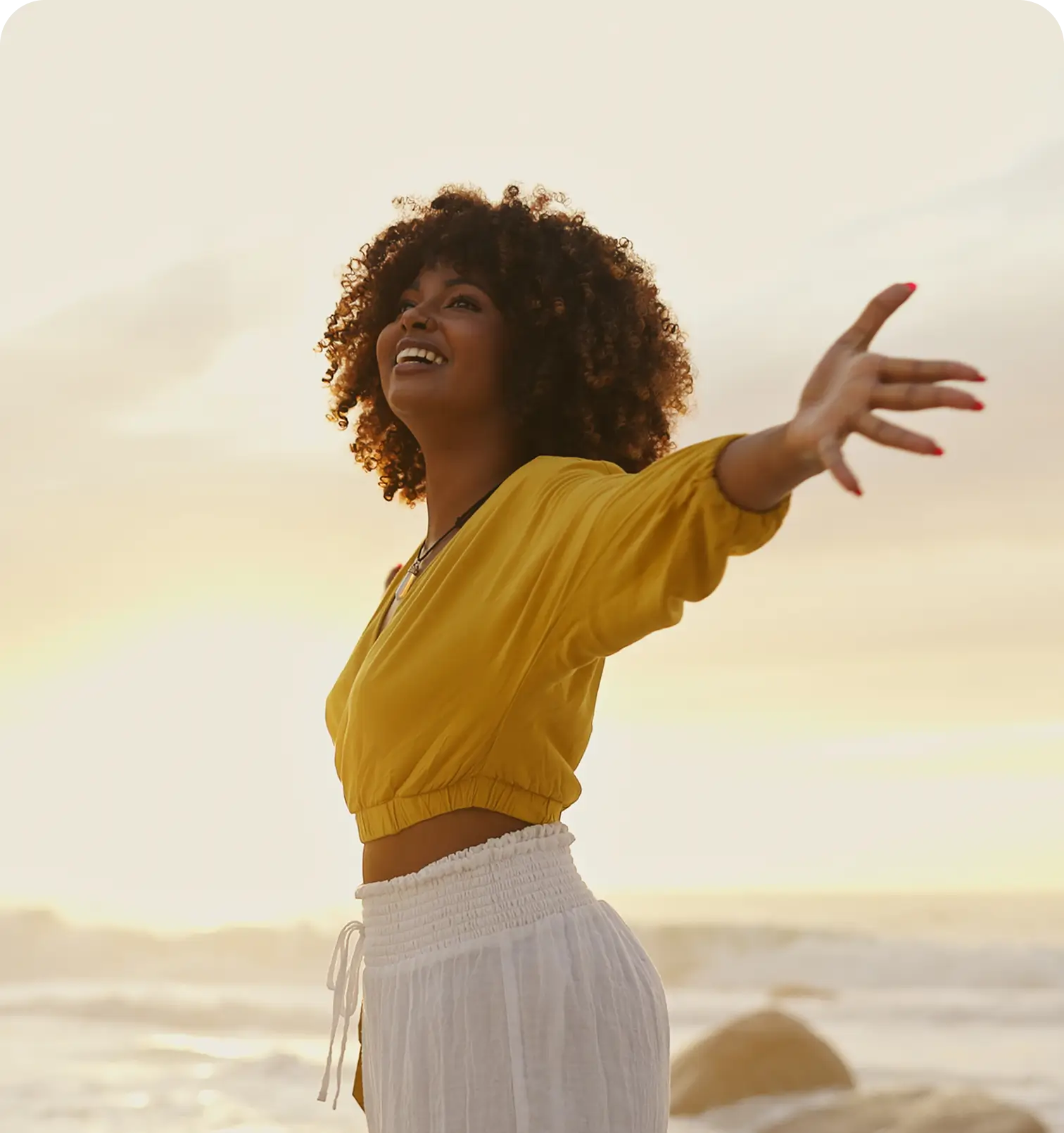 Woman joyfully spreading her arms by the beach at sunset.