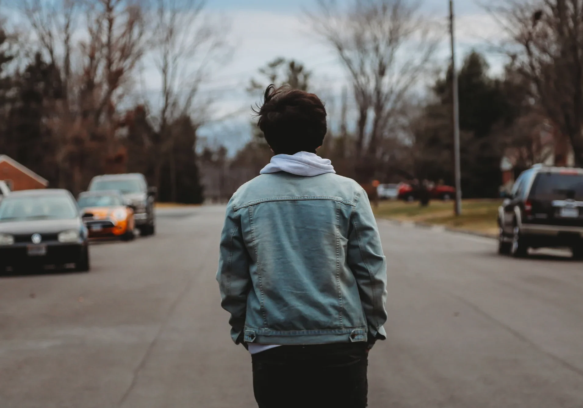 Person walking down a street wearing a denim jacket and hoodie.